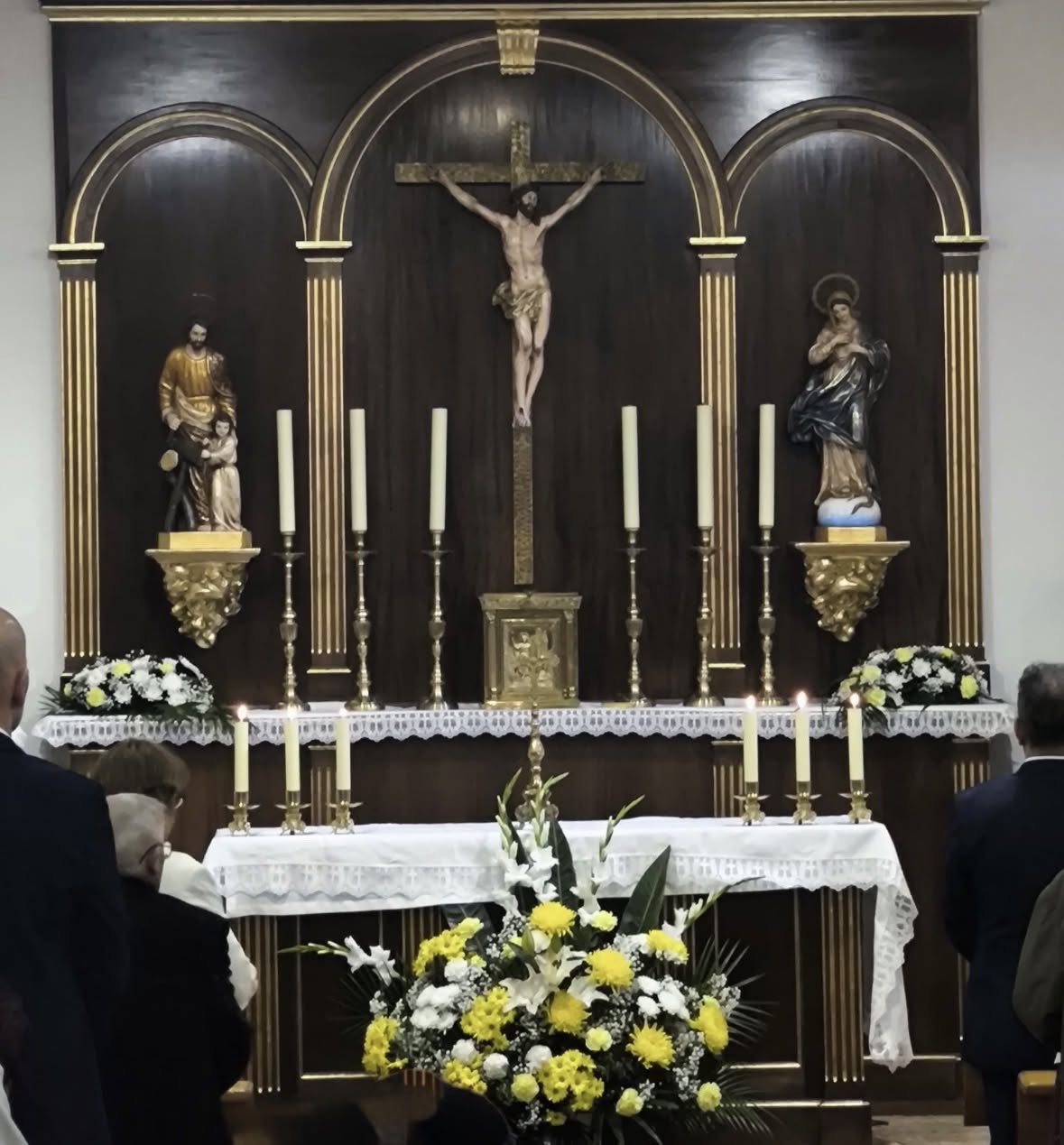 Altar y retablo de San Bernardo, con el crucifijo central, imágenes religiosas, velas y flores